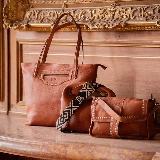 Trois sacs à main en cuir marron sur un meuble ancien en bois sculpté